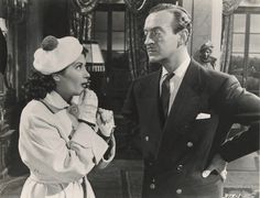 an old black and white photo of a man standing next to a woman wearing a hat