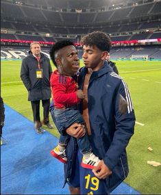 a man holding a small child in his arms at a soccer game with other people looking on