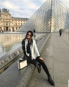 a woman sitting on the edge of a walkway next to a large pyramid in front of a building