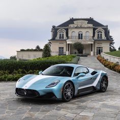 a blue sports car is parked in front of a large house on a cobblestone driveway