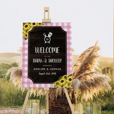 a welcome sign with sunflowers in the foreground and a pink checkered background