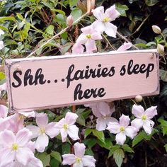 a pink sign that says she leaves sleep here with flowers in the foreground and bushes behind it