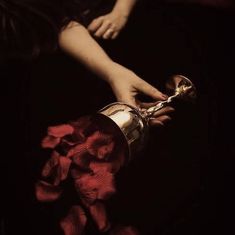 a woman's hands holding a wine glass with red flowers on it and the bottom half of her hand