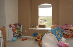 a child's room with toys and bookshelves on the floor, in front of a window