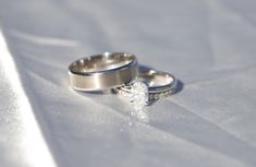 two silver wedding rings sitting on top of a white cloth covered tablecloth with a diamond in the middle