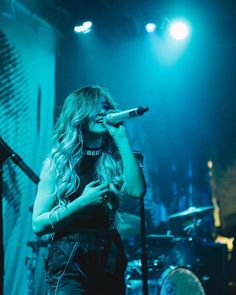 a woman singing into a microphone while standing in front of a drum set on stage