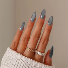 a woman's hand with grey and white nail polish on it, wearing a gold ring