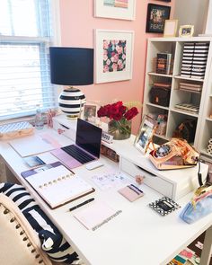 a white desk topped with a laptop computer next to a lamp and bookshelf