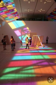 people are walking around in an art gallery with brightly colored light coming through the ceiling