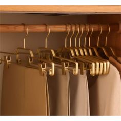 an assortment of clothes hanging on wooden hangers in front of a closet with beige curtains