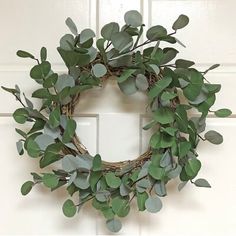 a wreath hanging on the front door with green leaves and branches attached to it's sides