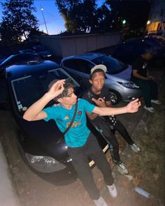 two men standing next to each other in front of parked cars