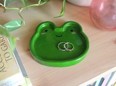 a green frog shaped dish with two wedding rings on it's ring holder next to some books