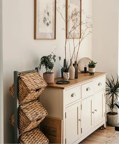 a room with some plants on top of a dresser and pictures hanging above the drawers