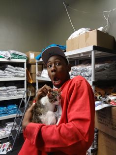 a man holding a cat in his hands while standing next to shelves full of shirts