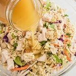 a bowl filled with salad and dressing being poured into the mixture to make chicken salad