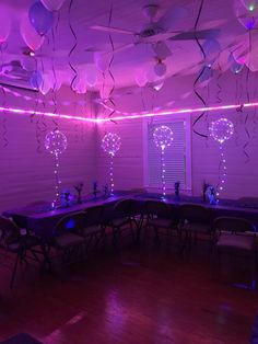 a room filled with lots of tables covered in purple lights and balloons hanging from the ceiling