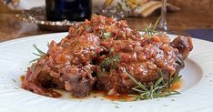 a white plate topped with meat covered in gravy next to a glass of wine