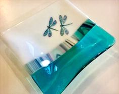 two dragonflys on a glass plate sitting on a white counter top with blue and green accents