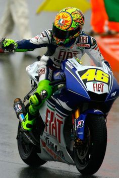 a man riding on the back of a motorcycle down a rain soaked road with his arms outstretched