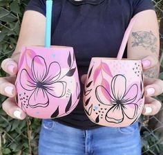 a woman holding two cups with flowers painted on them and a straw in her hand