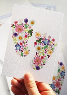 a person holding up a card with flowers on it in front of some envelopes