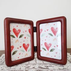 two small frames with hearts on them sitting on a doily covered tablecloth next to each other