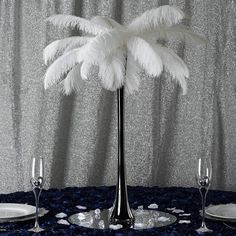 a table topped with plates and glasses next to a tall palm tree in front of a curtain