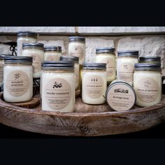 many jars are lined up on a wooden tray with labels and lids in front of a brick wall