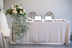 two laptops sitting on top of a table next to a vase with white flowers