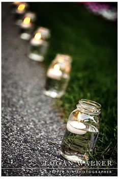 several mason jars filled with candles sitting on the side of a road next to grass