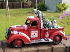 an old red truck with christmas trees in the bed is parked on a brick wall