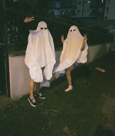 two people dressed in ghost costumes, one holding his hands up and the other reaching out