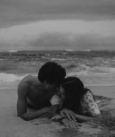 a man and woman laying on top of a sandy beach next to the ocean under a cloudy sky