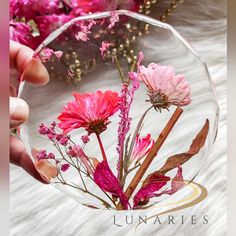 a hand holding a clear glass vase filled with pink flowers