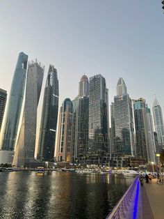 there are many tall buildings in the city next to the water and people walking on the sidewalk