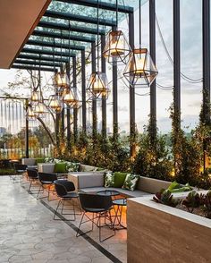 an outdoor dining area with tables and chairs, plants on the wall and lights hanging from the ceiling