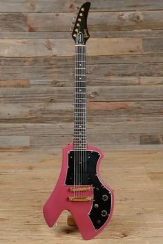 a pink and black guitar sitting on top of a wooden floor