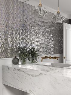 a bathroom with marble counter tops and gold accents on the wall, along with two hanging lights