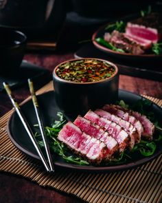 two plates with food on them and chopsticks next to one plate filled with meat