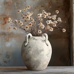 a vase filled with flowers sitting on top of a wooden table next to a rusted wall