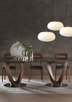 a glass table with four chairs and three lights hanging from it's sides, in front of a gray wall