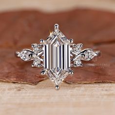 an emerald cut diamond ring on top of a wooden surface with leaves in the background