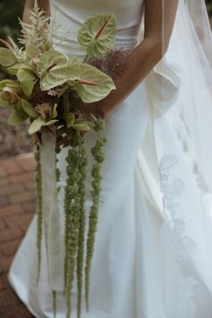 a woman in a wedding dress holding a bridal bouquet with greenery on it