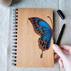 a hand holding a notebook with a blue butterfly on it and a pen next to it