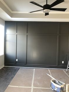 an empty room with black painted walls and ceiling fan in the corner, next to a ladder