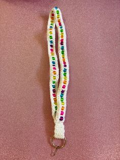 a white lanyard with multicolored beads hanging from it's side on a pink surface