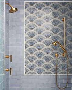 a bathroom with blue tile and gold faucet shower head, hand held showerhead, and tiled walls