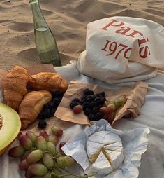 there are many fruits and pastries on the beach with a bottle of wine in the background