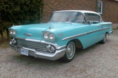 an old blue car parked in front of a brick building